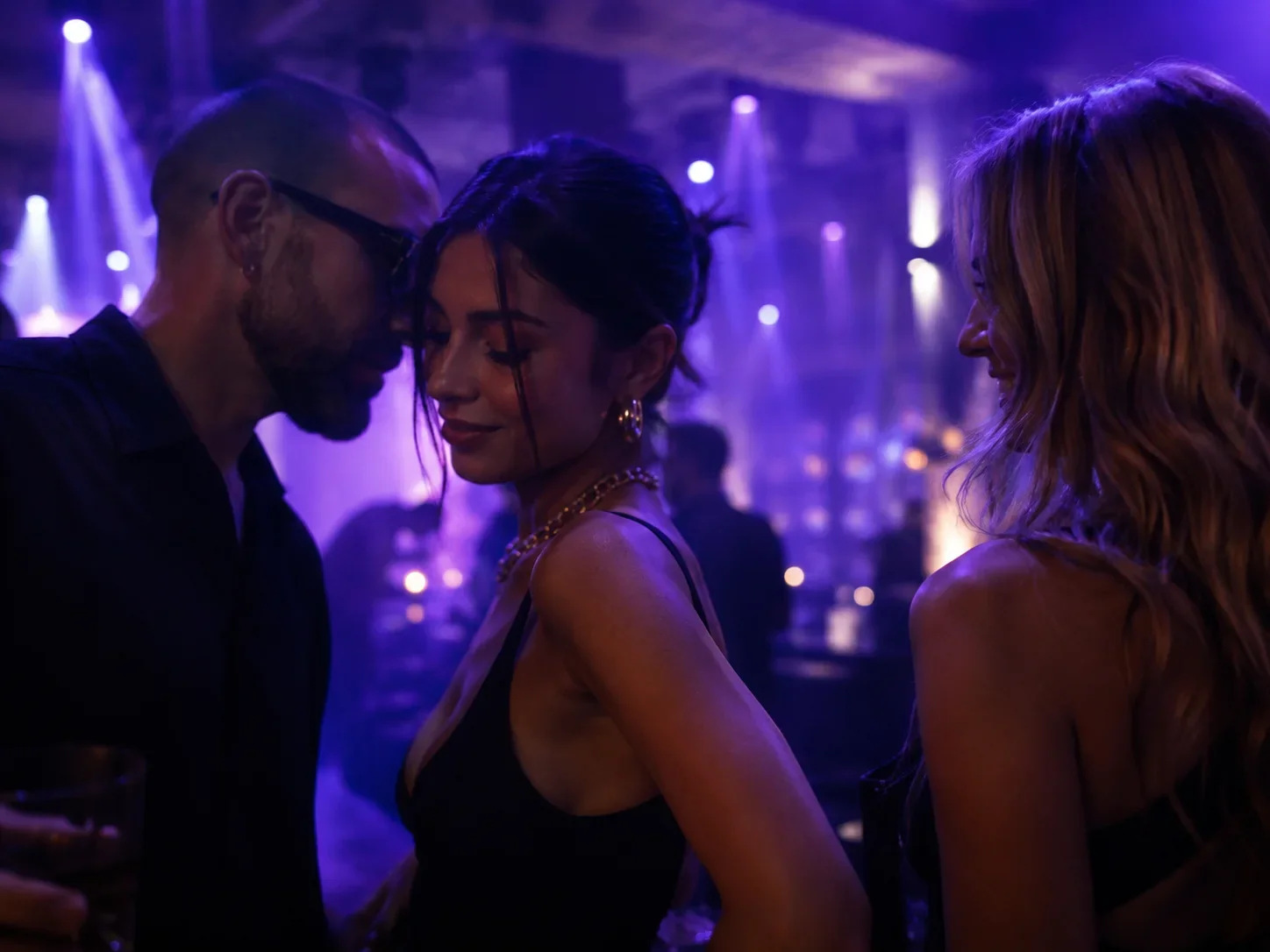 Drei Partygäste genießen einen persönlichen Moment mitten im violett beleuchteten Club.