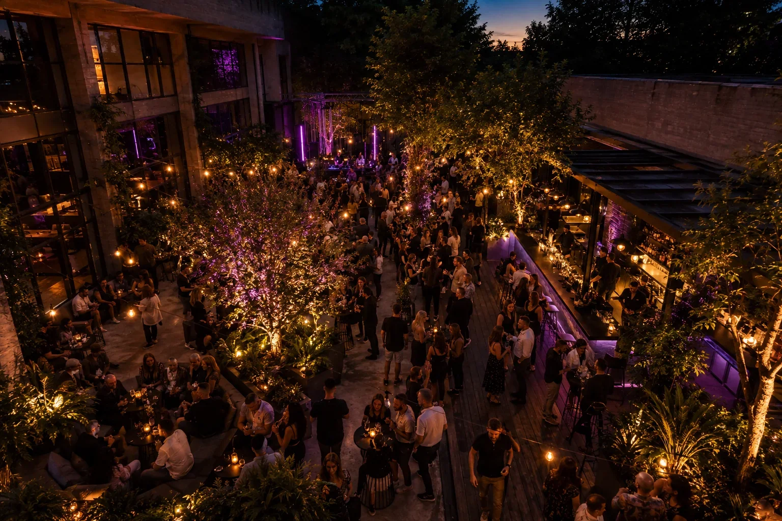 Ausgelassene Afterwork-Gäste tanzen beim Sonnenuntergang unter Lichterketten auf dem Gartenfloor.